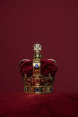 Golden crown on a velvet cushion on a deep red background with copy space in a vertical image
