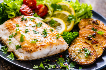 Fish dish - fried cod fillet with potatoes and vegetables on wooden table