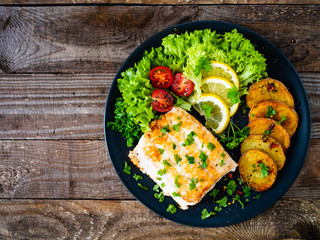 Fish dish - fried cod fillet with potatoes and vegetables on wooden table