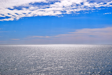 View of the blue sky with white clouds over the silvery sea. The water glistens in the sun.