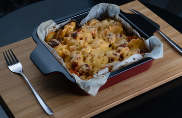 golden crispy skin chicken grilled in oven with potato wedges and leek in cast iron pan on old wooden boards, chopping board with slices of onion and cherry tomatoes on background