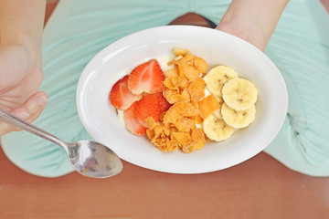 Woman holding Cornflakes cereal with strawberries and banana in a white bowl