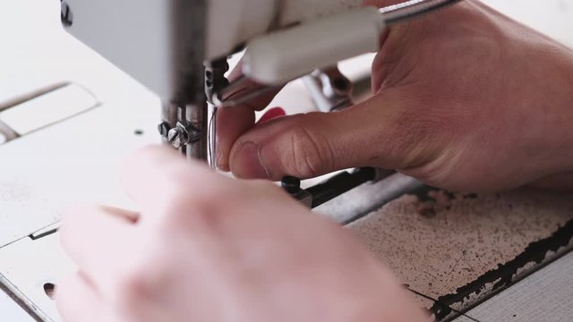 The master is preparing a sewing machine for work. The leather-dresser is putting thread through a needle.