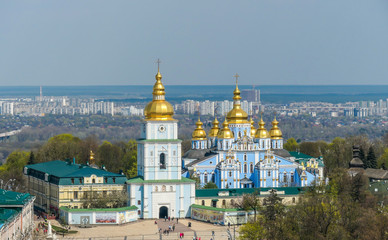 Fototapeta na wymiar Distanced view on St Michael's Golden-Domed Cathedral in Kiev, Ukraine. The walls of the cathedral are painted blue and nicely decorated on each facade. Golden domes are reflecting the strong sun.