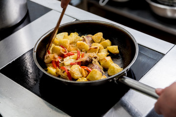 Chef cooks fried potatoes with pieces of meat in a restaurant kitchen