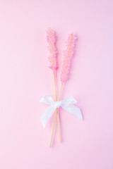 Two pink rock candy on pink paper background decorated with a white bow, vertical, top view