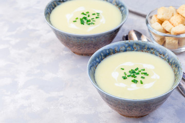 Potato leek soup in a blue ceramic bowl garnished with green onion served with croutons, horizontal, copy space