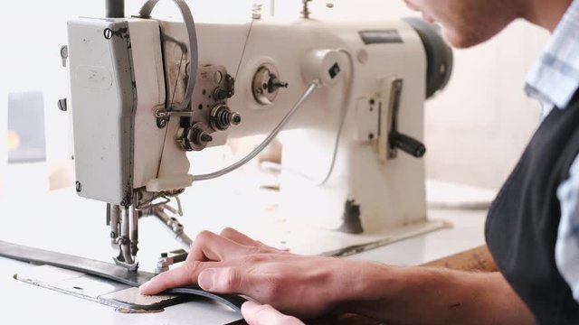 A craftsman stitches a men's leather belt on a sewing machine