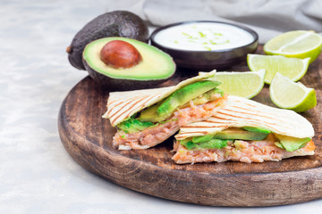 Grilled quesadilla with smoked salmon and avocado served with yogurt and lime dip, on wooden board, horizontal, copy space