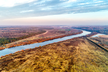 The bend of a wide river flowing among fields and forests. Autumn landscape, aerial view.