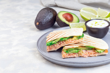 Grilled quesadilla with smoked salmon and avocado served with yogurt and lime dip, on gray plate, horizontal, copy space