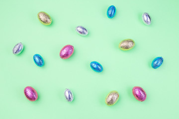 Green paper texture many colorful chocolate candy eggs, Easter background or pattern in pastel colors,  horizontal