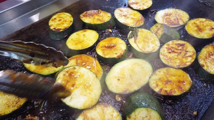 Roasting round slices of zucchini, vegetarian cuisine. The cook flips the fried slices to the other side.