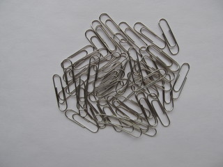 Chaotically laid out metal paper clips on a light background. Office supplies.