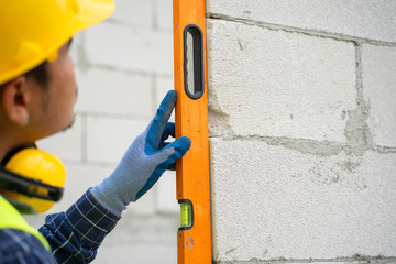 Engineer measures the work out wall lightweight concrete blocks with a level at construction site.