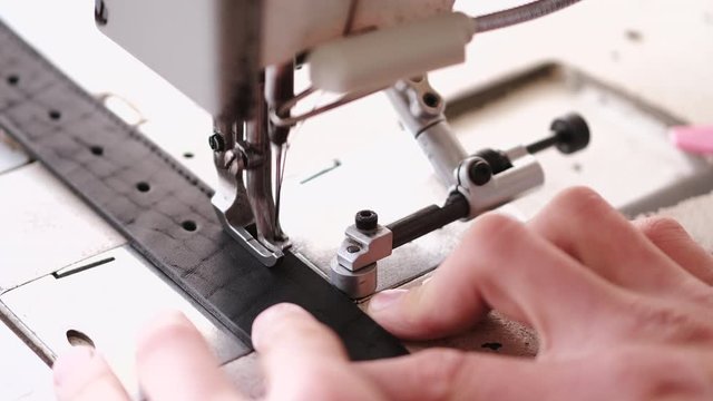 A craftsman stitches a men's leather belt on a sewing machine