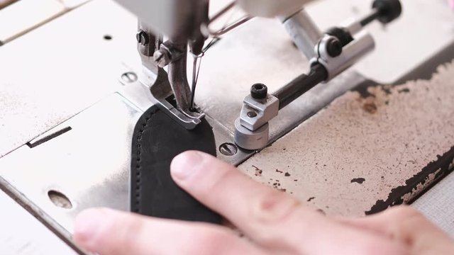 A craftsman stitches a men's leather belt on a sewing machine