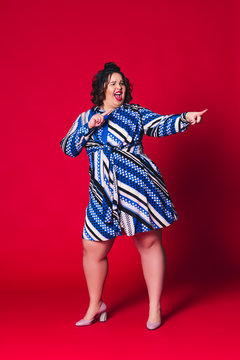 Happy plus size model in blue dress, fat woman dancing on red background