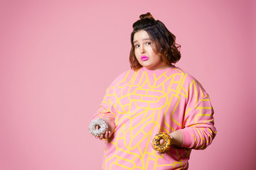 Sad plus size model with doughnuts, fat woman sadness and overeats on pink background