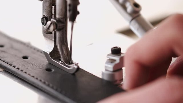 A craftsman stitches a men's leather belt on a sewing machine