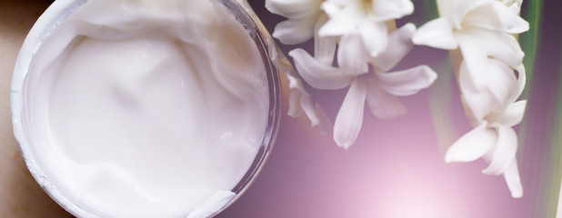 Face cream and white spring flowers, top view
