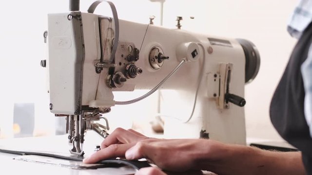 A craftsman stitches a men's leather belt on a sewing machine