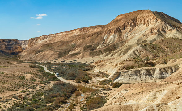 a single tour bus on the road to the ein avdat national park in israel with the canyon and mountains in the background and the nahal zin stream bed in the foreground