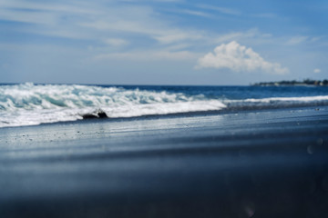 The black sand of Goa Lawah beach in Bali. The wave rolls on the shore.