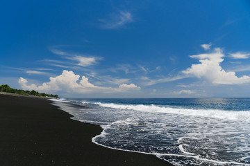 Wave on the black sand of Goa Lawah beach in Bali. The wave rolls on the shore.