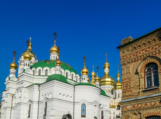 Fototapeta na wymiar A close-up view on Pechersk Lavra in Kiev, Ukraine, known as the Kiev Monastery of the Caves. Historic Orthodox Christian monastery. Green rooftops with golden domes. Walls are painted white.