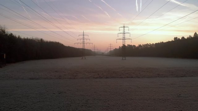 Flying backwards removing from power lines in sunrise back light, public infrastructure for electricity distribution across countryside environment