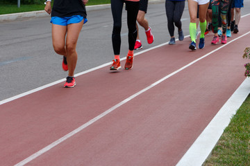 A group of athletes running on a track in a park. Only legs are visible.
