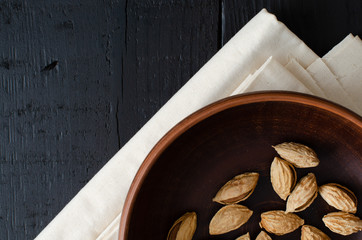 almonds in nutshell on clay dish on linen. Black background. Top view with copy space