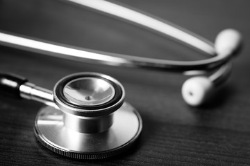 Close-up of a doctor’s stethoscope sitting on dark wooden desktop.