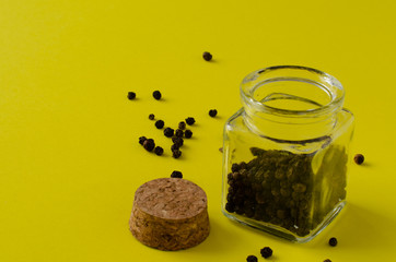 Black pepper in small glass bottle on yellow background