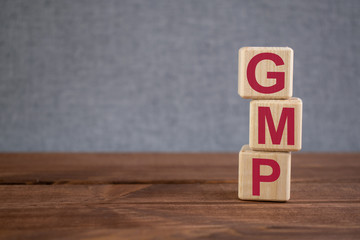 GMP (Good Manufacturing Practice) acronym on wooden cubes on dark wooden backround. Business concept.