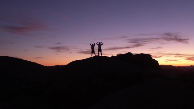 Aerial, tracking, drone shot of silhouette men dancing on a hill, in front of a cityscape, dusk sky, in Los Angeles, California, USA