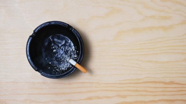 Cigarette in the ashtray on wooden table, overhead view
