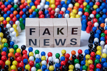 fakenews text on wooden cubes, surrounded by wooden figurines in several colours
