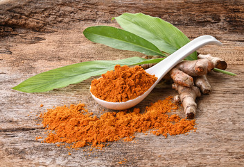 Turmeric powder and fresh turmeric on wooden background.