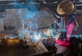 Double exposure of welder are welding a steel structure work with process Flux Cored Arc Welding(FCAW)and dressed properly with personal protective equipment(PPE)for safety with power plant background