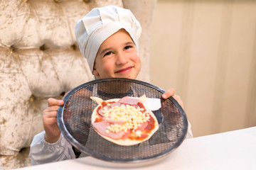 Cook boy. Little boy is a cook in flour in a white hat and apron in the kitchen preparing homemade pizza