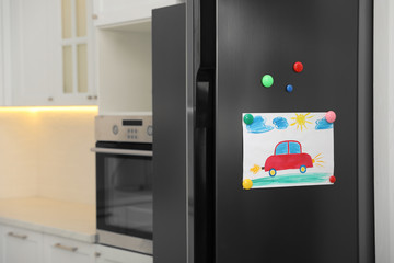 Modern refrigerator with child's drawing and magnets in kitchen