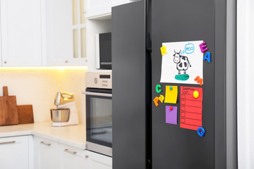 Modern refrigerator with child's drawing, notes and magnets in kitchen