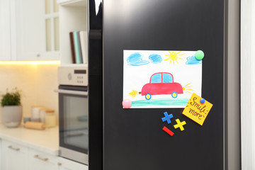 Modern refrigerator with child's drawing, note and magnets in kitchen