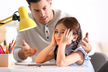 Father scolding his daughter while helping with homework at table indoors