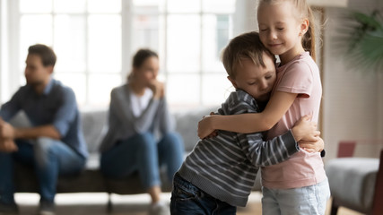 Stressed little girl embracing smaller brother, overcoming parents argue divorce together. Unhappy frustrated kids siblings suffering from family quarrels, misunderstanding of father and mother.