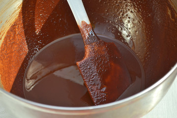 Melted delicious brown chocolate in a metal bowl for future handmade sweets, with a mixing spatula