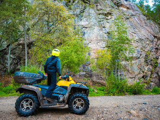 ATV ride. ATV driver looks at the sky. Biker stopped and admires the sky. ATV on the background of the mountain in the forest. Biker admires the top of the mountain. Yellow quadricycle.