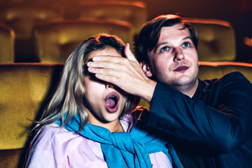 A couple watching a thriller movie in the cinema, Men use their hands to close his girlfriend's...